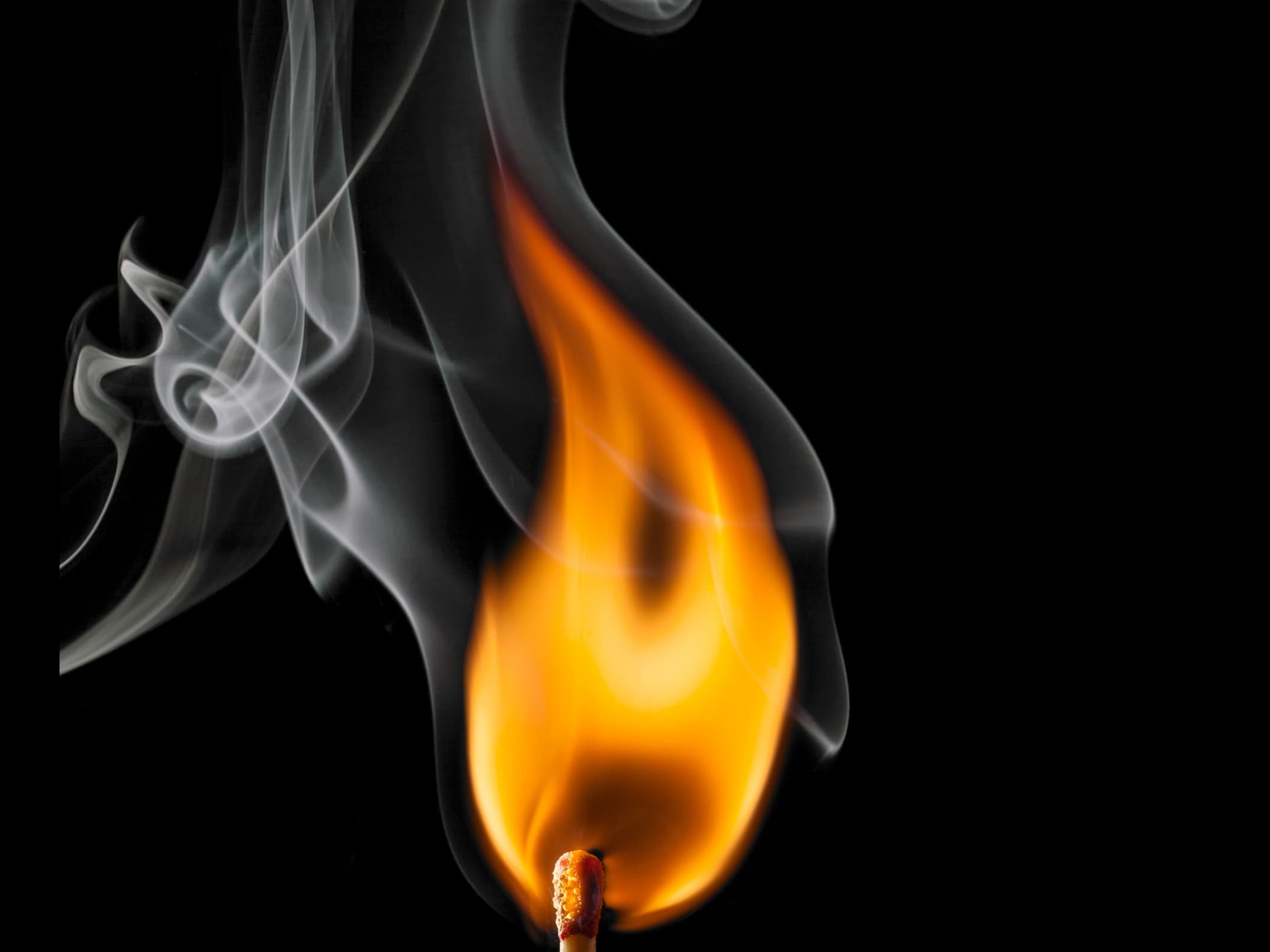 A single lit match with smoke curling above the flame against a black background, representing the difference between real charge and sudden reactive shock.