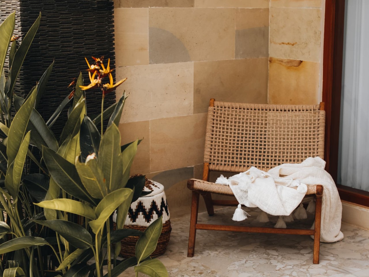 A soft tasseled throw draped loosely over a woven chair on a warm terracotta patio, representing gently setting down what isn't yours to carry.